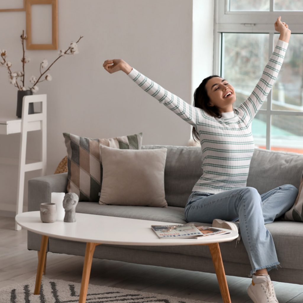 Young woman stretching on grey couch in living room